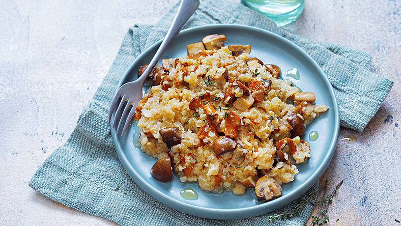 Teller mit Blumenkohlrisotto und Pilzen auf Tuch und Glas