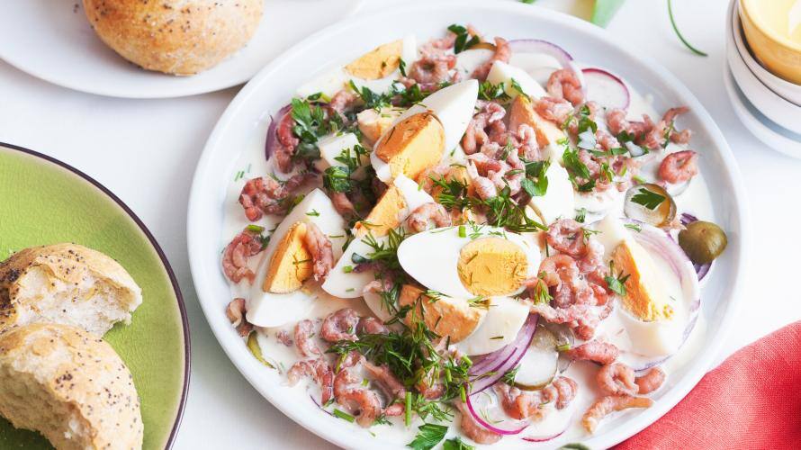 Teller mit Eiersalat, Krabben und Kräutern, daneben Brötchen