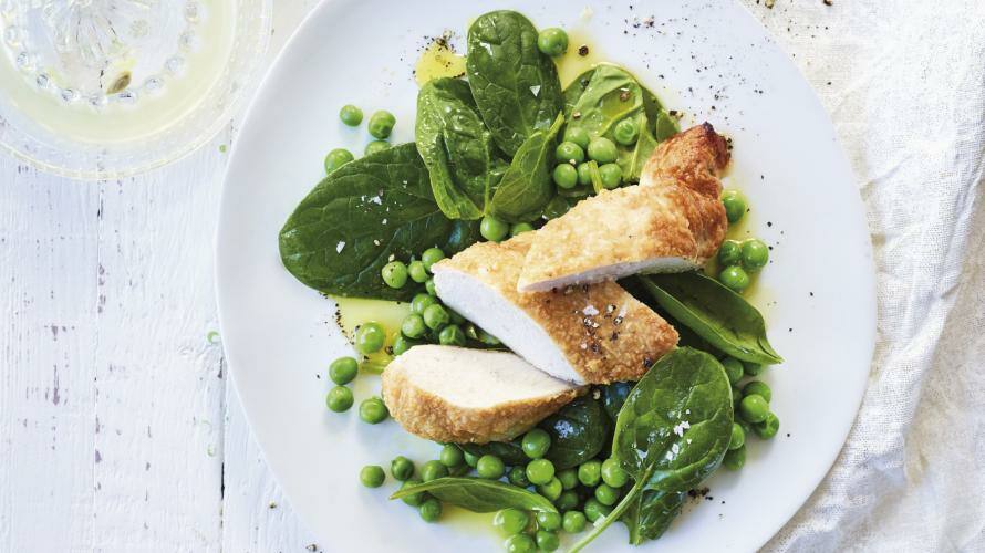 Parmesanhähnchen mit Erbsen und Spinatsalat auf einem weißen Teller