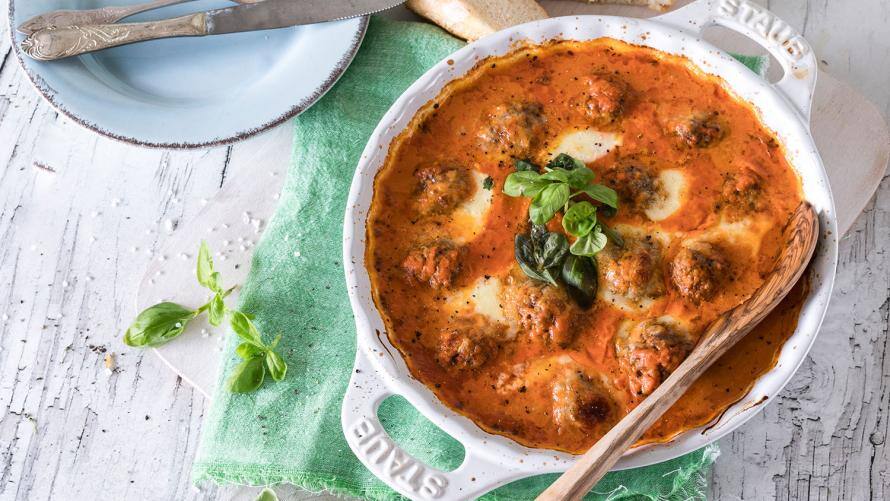 Weißer Topf mit Hackbällchen in Tomatensauce, darüber Basilikum