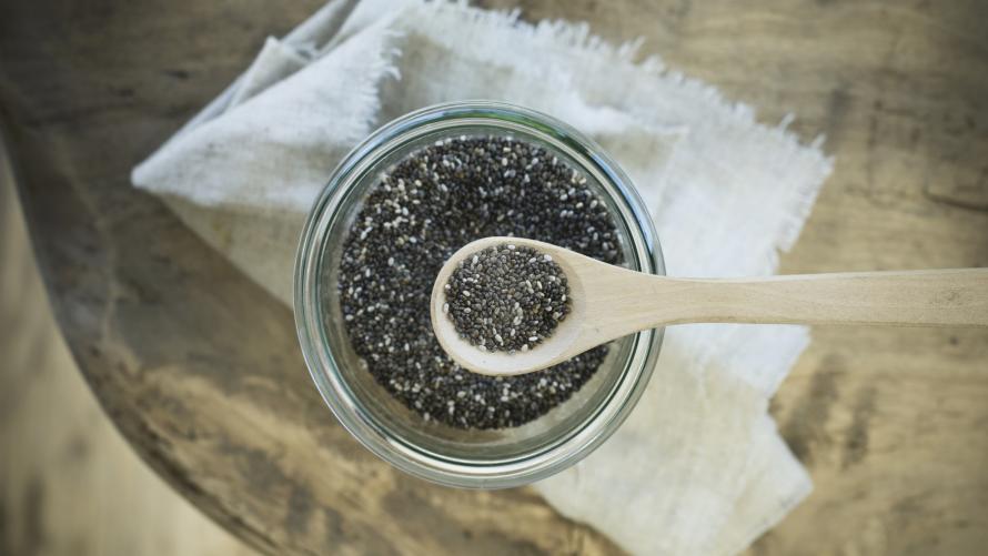 Chiasamen auf einem Holzlöffel und Vorratsglas auf rustikalem Holztisch