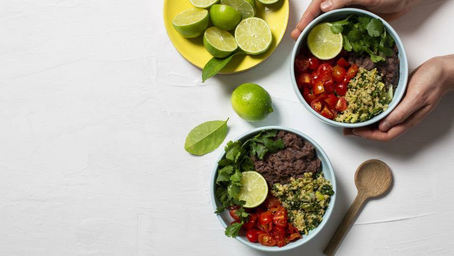 Vegane Bowl mit Bohnenmus und Blumenkohlreis, daneben aufgeschnittene Limetten