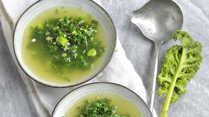 Zwei Schüsseln mit Brühe und Grünkohl auf weißem Tuch, daneben frischer Grünkohl