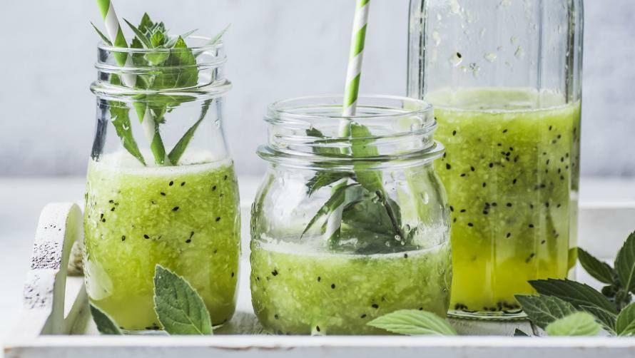 grüner Smoothie in Gläsern und Flasche, in den Gläsern sind Strohhalme und dekorative Minze