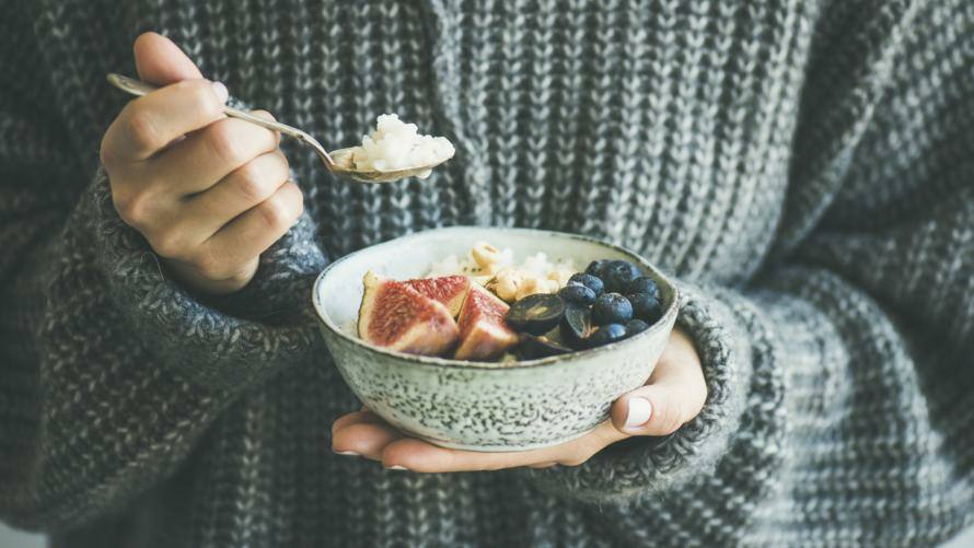 Frau mit Strickpulli hält Schüssel mit Frühstück 