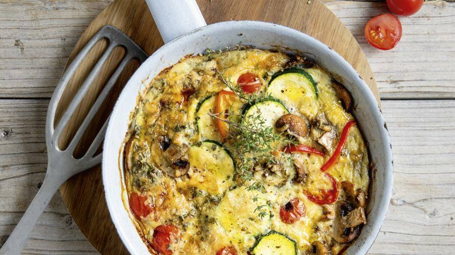 Helle Pfanne mit Gemüse-Frittata auf Brett, daneben Pfannenwender