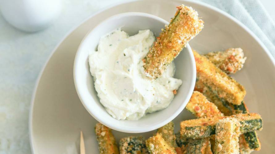 Weißer Teller mit panierten Zucchinisticks, dazu Mayonaise im Schälchen