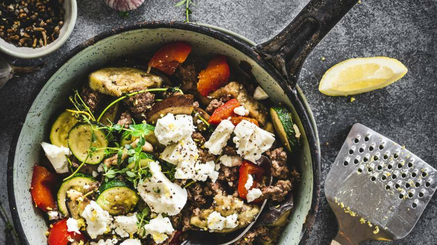Pfanne mit Hackfleisch, Paprika, Feta, Zucchini, Aubergine und Zitronenspalten, darüber Kräuterzweige