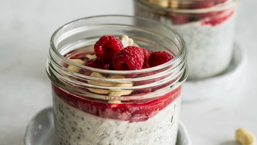 Gläschen mit Chiapudding, Himbeercreme, Himbeeren und gehackten Cashewkernen