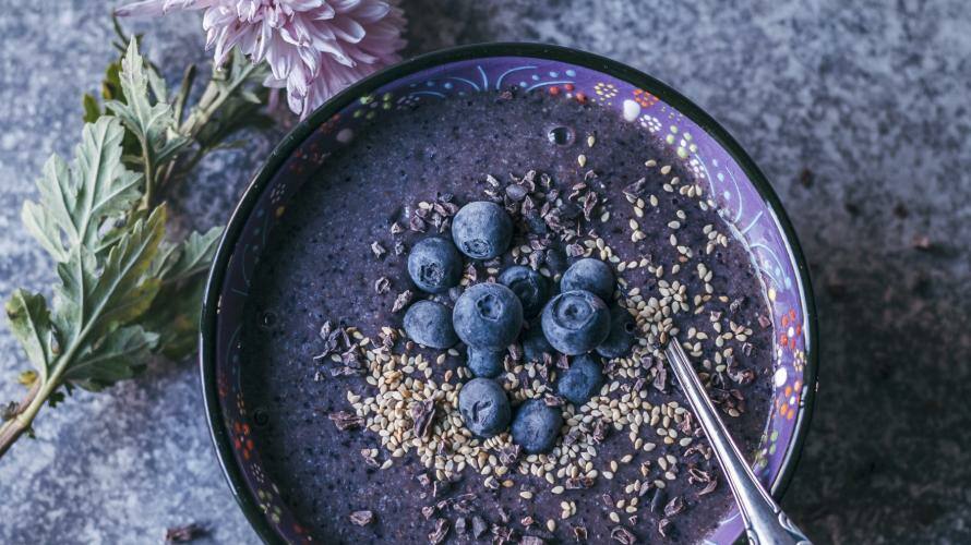 Schüssel mit lila-farbener Smoothie, darüber Beeren, Kakao Nibs und Sesam