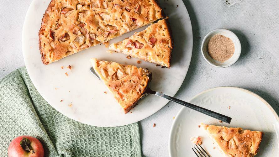 Apfelkuchen auf einer Servierplatte, Teller mit Kuchenstücken daneben