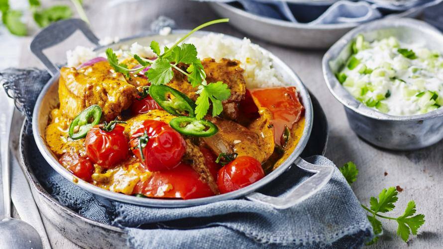 Buntes Curry mit Hähnchen in einer Schale, daneben Blumenkohlreis