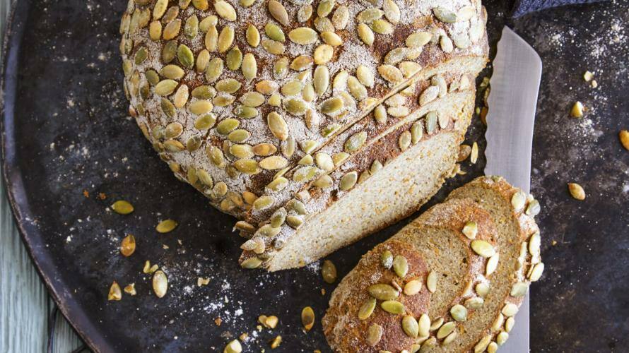 Angeschnittener Brotlaib auf dunklem Teller, darüber Kürbiskerne