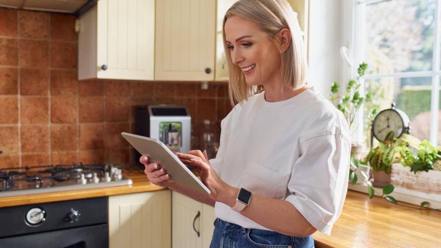 Eine Frau steht in der Küch und plant mit der Low-Carb-App auf dem Tablet ihre Ernährung der nächsten Woche