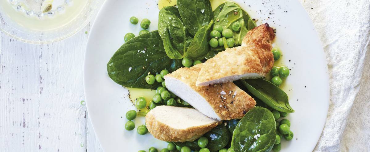 Parmesanhähnchen mit Erbsen und Spinatsalat auf einem weißen Teller