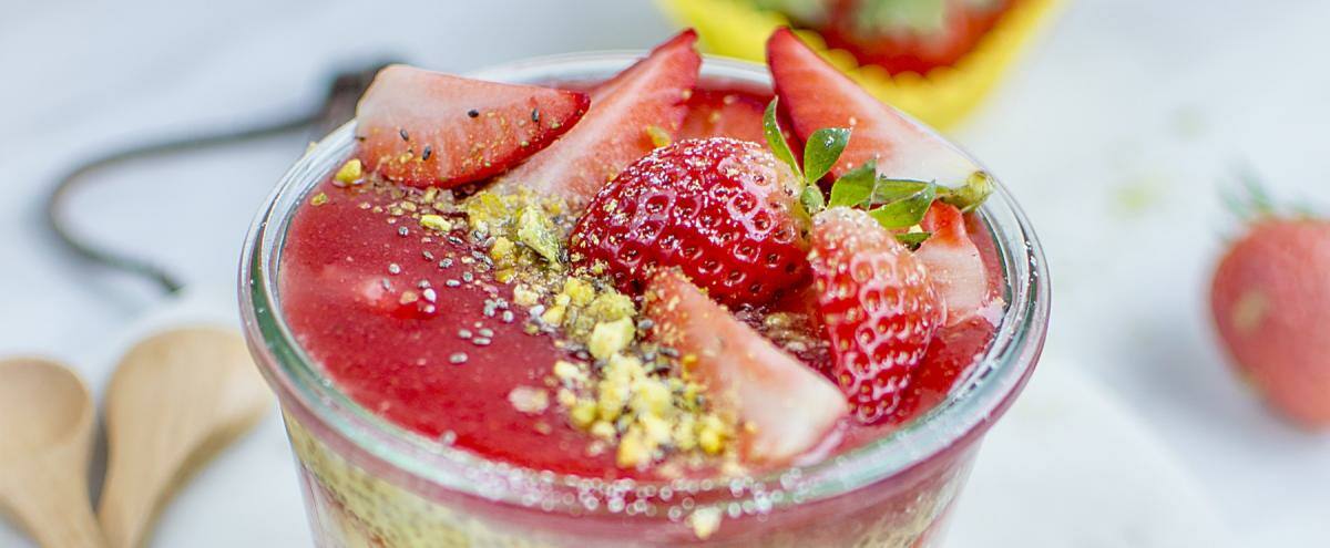 Weckglas mit Pudding und Erdbeeren auf Brett und Kochlöffel 