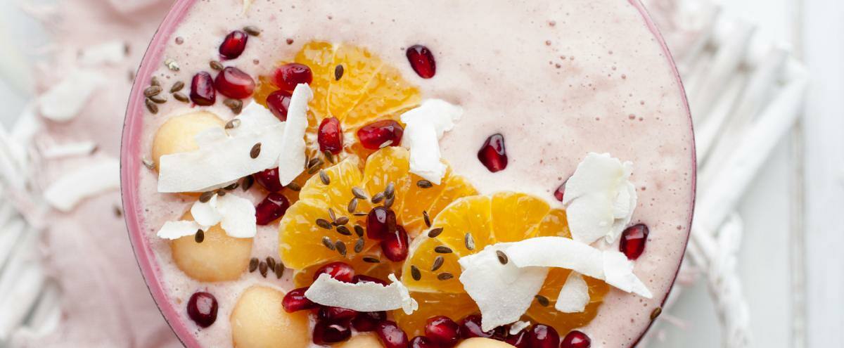 Becher auf einem Tuch mit Orangen,Kokosraspeln, Granatapfel und Melone