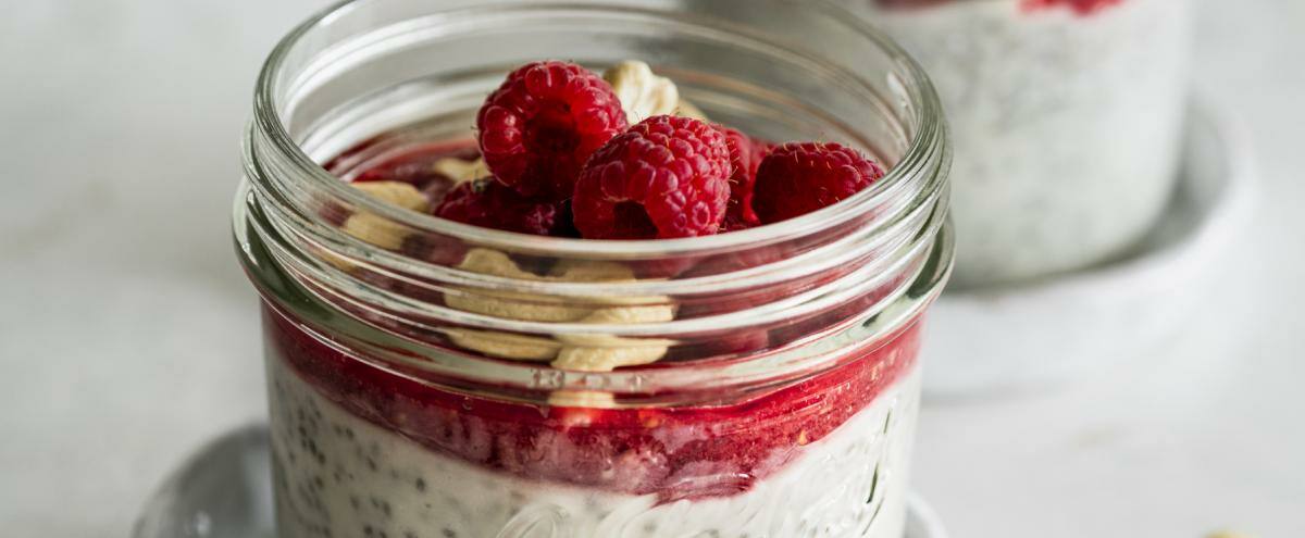 Gläschen mit Chiapudding, Himbeercreme, Himbeeren und gehackten Cashewkernen