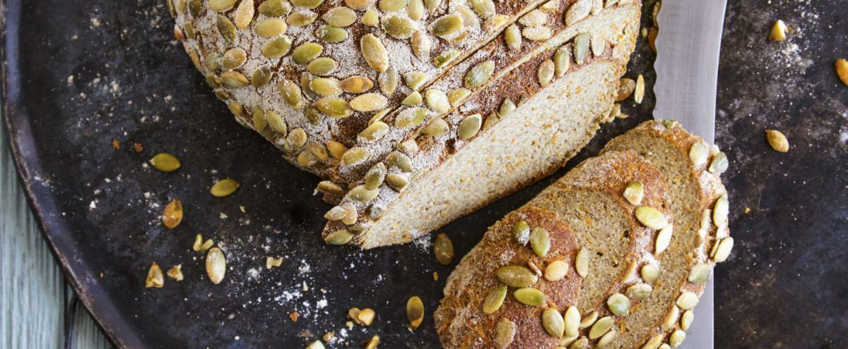 Angeschnittener Brotlaib auf dunklem Teller, darüber Kürbiskerne
