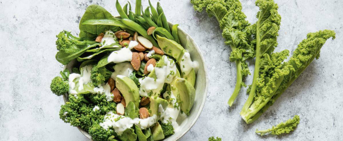 Bowl mit Grünkohl, Brokkoli, grünen Bohnen, Babyspinat, Avocado und Mandeln, darüber Joghurt-Dressing