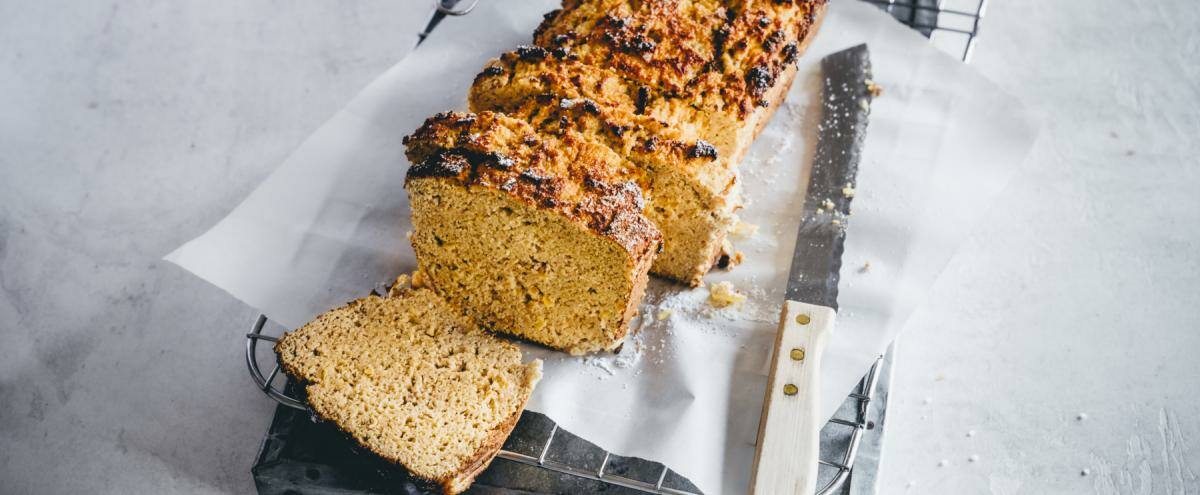 Angeschnittenes orangenes Brot auf weißem Papier, daneben großes Schneidemesser