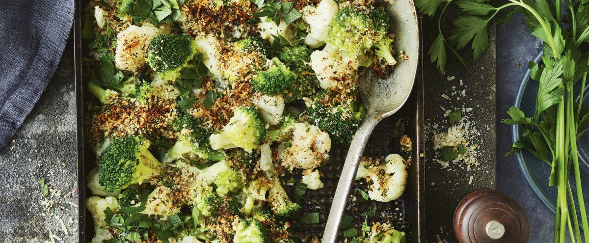 Brokkoli- und Blumenkohlröschen in Auflaufform, darüber gemahlene Haselnuss und Parmesan
