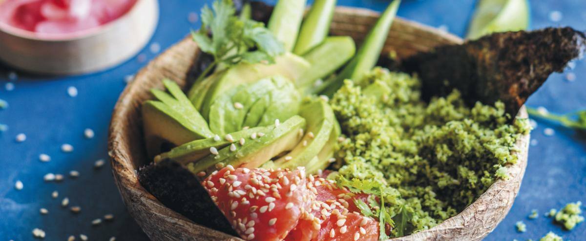 Schale mit Brokkolireis, Lachs und Avocado auf einem Tisch