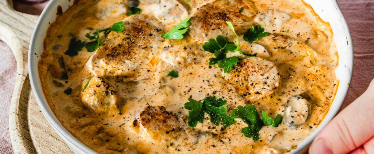 Auflaufform mit Rahmsoße und Schweinefilets wird auf einen Tisch gestellet