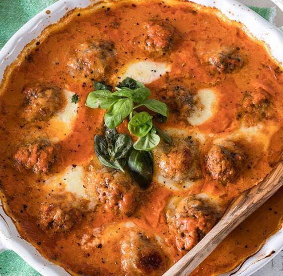 Weißer Topf mit Hackbällchen in Tomatensauce, darüber Basilikum