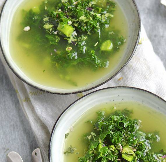 Zwei Schüsseln mit Brühe und Grünkohl auf weißem Tuch, daneben frischer Grünkohl