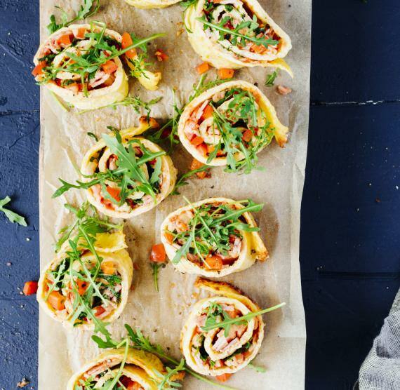 Pizza-Schnecken mit Schinken und Paprika auf einem Holzbrett mit Tuch.