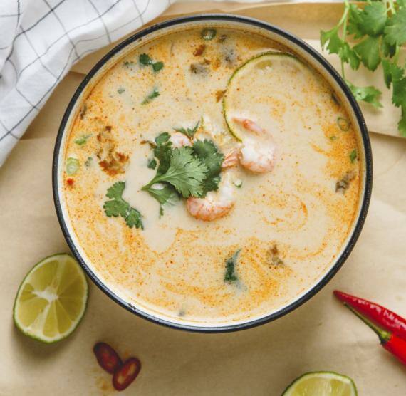 Schale mit Suppe auf Brett, daneben Limette, Chili und Koriander