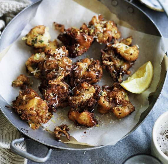 Frittierter Blumenkohl im Teigmantel mit Speck auf Küchenkrepp, daneben eine Zitronenspalte