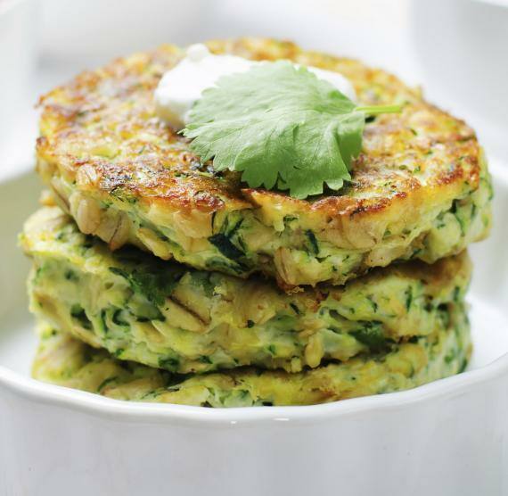 Weiße Form mit gestapelten Zucchinipuffern, darüber Saure Sahne und Koriander