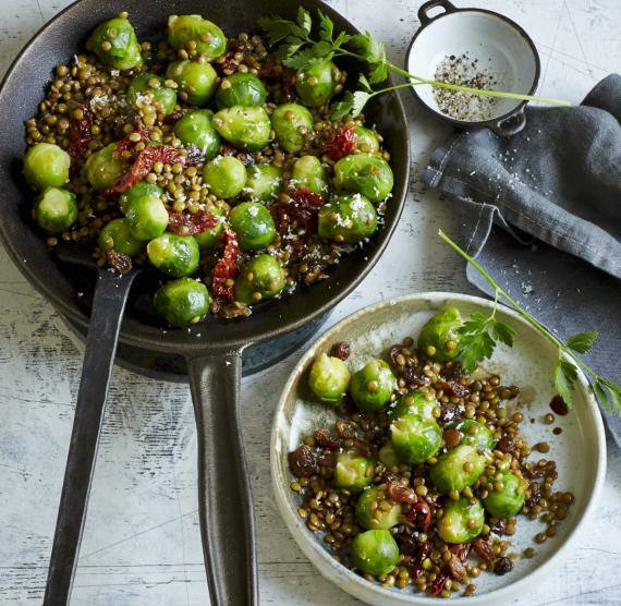Pfanne und Teller mit Rosenkohl, Berglinsen und getrockneten Tomaten, daneben Stängel Petersilie und Schälchen mit Pfeffer