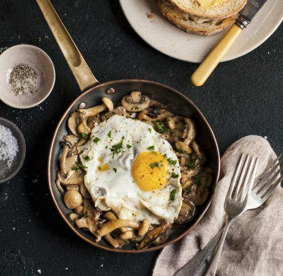 Gebratene Pilze mit Spiegelei ind Pfanne, daneben Toast mit Butter