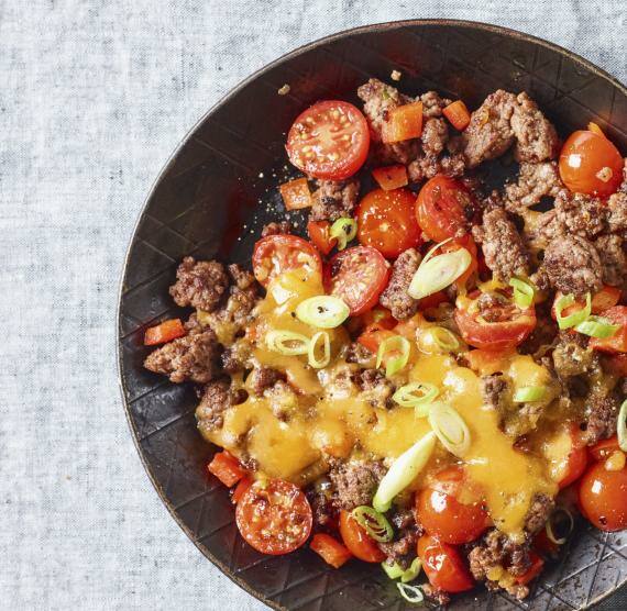 Hack-Pfanne in einer Eisenpfanne, daneben ein Schälchen mit Lauchzwiebeln