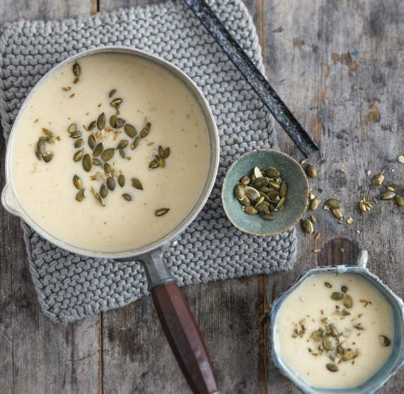 Topf mit cremefarbener Suppe, darüber Kürbiskerne und Fenchelsamen