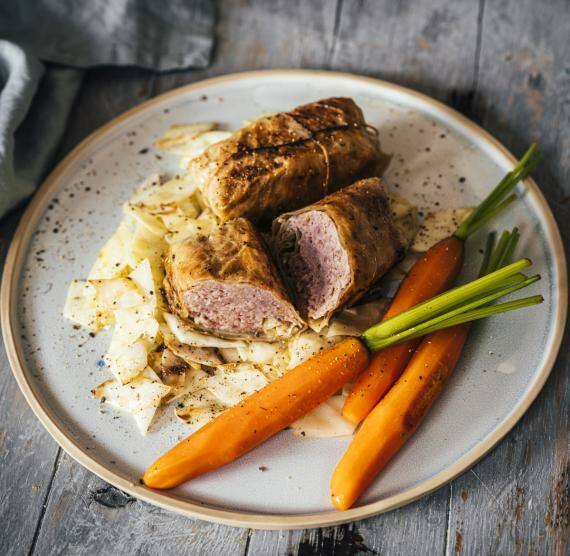 Kohlrouladen auf Weißkohl, dazu Karotten auf einem hellen Teller, der auf einem Holzuntergrund steht