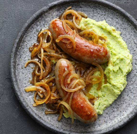 Grünes Rosenkohlpüree mit Bratwürsten auf einem dunklen Teller