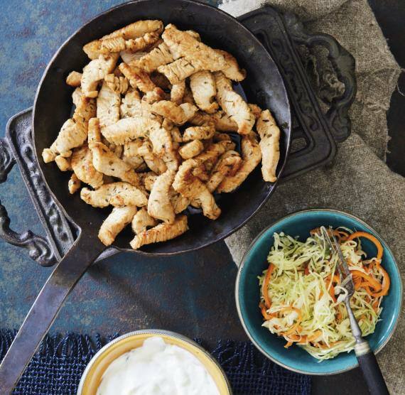 Gyros in einer Pfanne, daneben eine Schale Krautsalat und eine Schale Dip auf einem Tisch