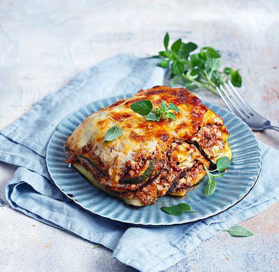 Teller mit Lasagne auf Tuch mit Gabel und Basilikum