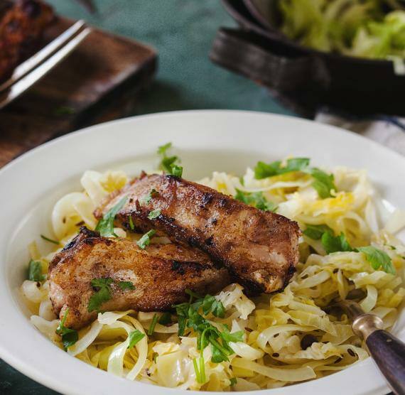 Rippchen auf Brett mit Gabel, Teller mit Kohl und Rippchen