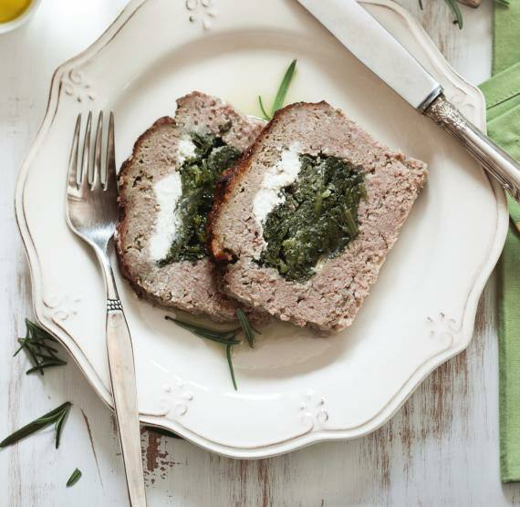 Hackbraten auf Brett und Teller mit Käse und Spinat, Messer und Gabel