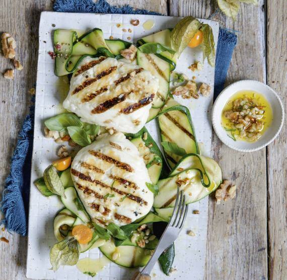 Brett mit gegrilltem Halloumi auf Zucchini und Basilikum, dazu gehackte Nüsse und Öl