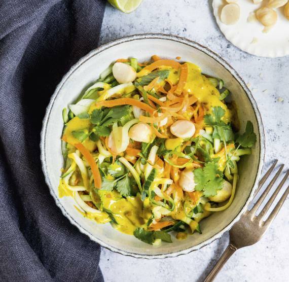 Schale mit Gemüsenudeln, gelbem Dressing, Macadamianüssen und Koriander