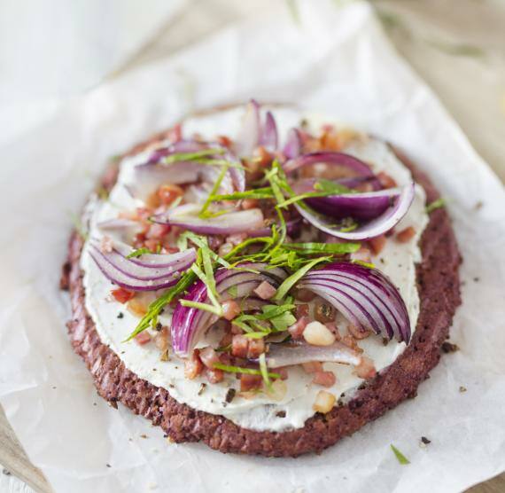 Runder, rötlicher Flammkuchen mit Schmand, Speck, roten Zwiebeln und Petersilie