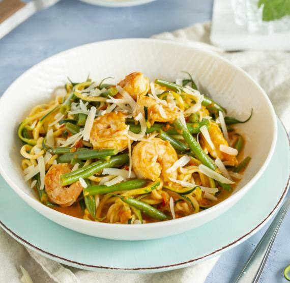 Weißer Teller mit Zucchininudeln, grünen Bohnen, Garnelen und heller Sauce