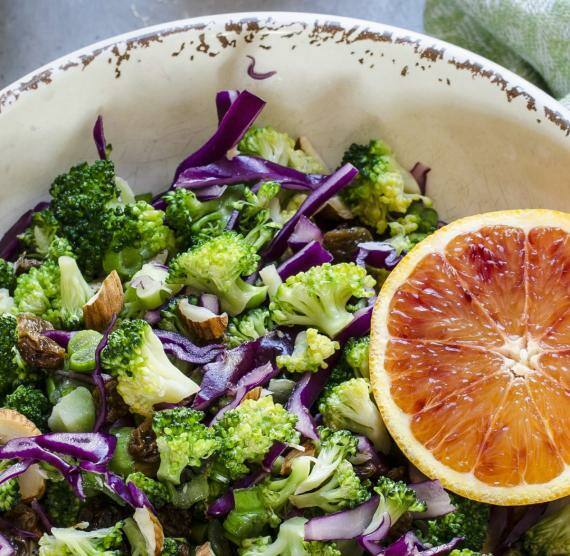 Schüssel mit Salat aus Brokkoli und Rotkohl, dazu Mandeln, Rosinen und eine halbe Blutorange