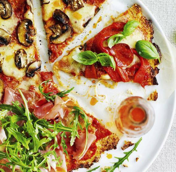 Weißer Teller mit Pizza, belegt mit Champignons, Schinken, Käse und Rucola